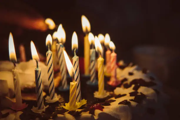 Photo of anniversary cake with hand burning candles in dark