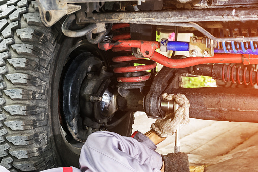 Car mechanic in grey uniform using a wrench to tighten the nut under the car for maintenance, Automotive industry and garage concepts.