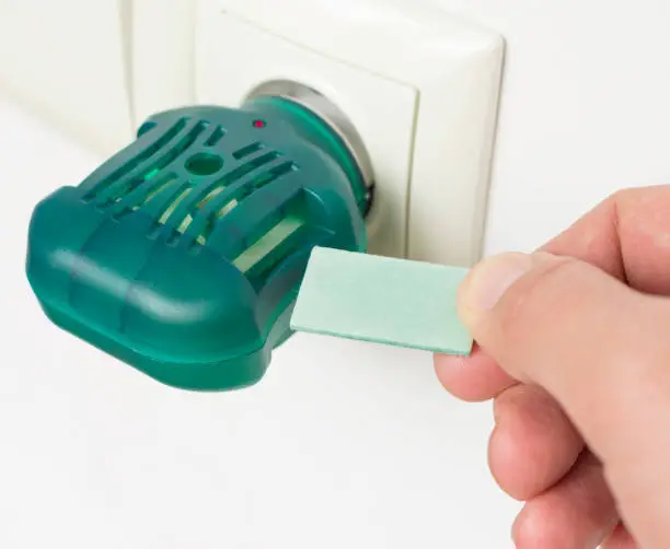 Men's hand with plate of electric anti-mosquito fumigator in the socket. Electric mosquito repellent. Selective focus.