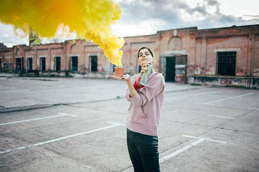 Hipster girl with spray can and yellow smoke bomb. Street artist with spray bottle.