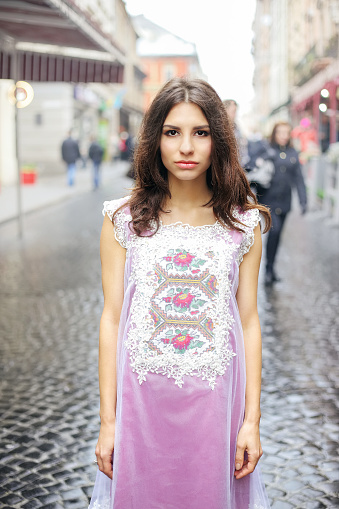 Young eastern woman in pink lace dress posing on the city street. Cute woman with long wavy hair walking in the city. Fashionable street look