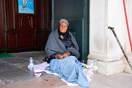 Destitute old lady sitting in the Santa Maria church doorway, Lagos, Algarve, Portugal, Europe.