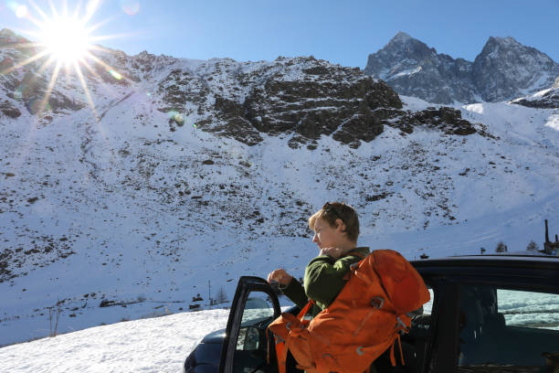 istock Young man throws on backpack by car parked in mountains 934108482