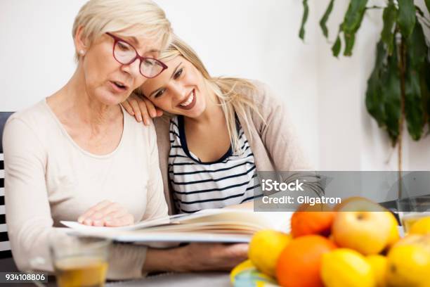 Young Woman Resting Her Head On Mothers Shoulder While Looking At Family Photo Album Stock Photo - Download Image Now