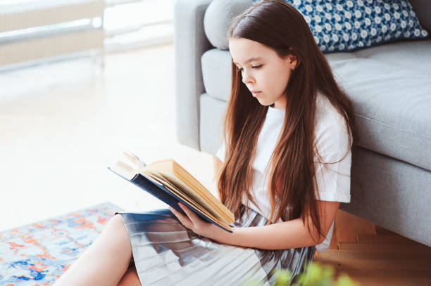 istock smart kid girl reading interesting book  at home, sitting with couch on background. Learning and education concept 934120214
