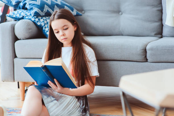 istock smart kid girl reading interesting book  at home, sitting with couch on background. Learning and education concept 934120230