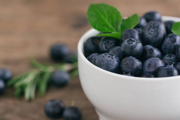 Fresh blueberries heap in white bowl in close up view macro concept with copy space on wood table for background. Blueberry is healthy and delicious fruits which have high antioxidant and vitamin C. montón de arándanos frescos en tazón de fuente blanco en cierre concepto macro de vista con espacio de copia en mesa de madera para el fondo. arándanos son frutas deliciosas y saludables que tienen altas propiedades antioxidantes y vitamina c.