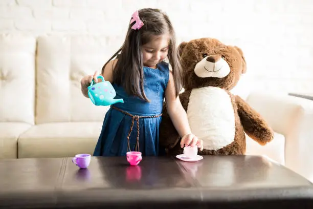 Portrait of cute little girl playing with a tea set on the table in living room, she is pouring tea in cups.