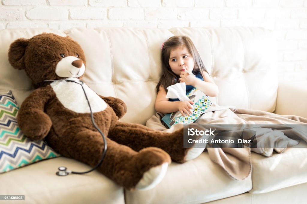 Ragazza malata con orsacchiotto medico sul divano - Foto stock royalty-free di Bambino