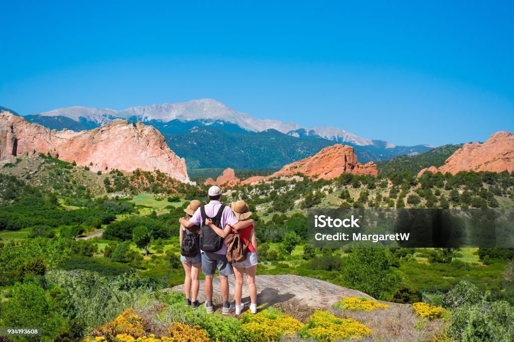 Happy family enjoying beautiful mountain view on vacation hiking trip. Happy family with arms around each other enjoying beautiful mountain view on  hiking trip. Beautiful red mountains and green hills in Colorado. Garden of the Gods, Colorado Springs, Colorado,  USA. Colorado Springs Stock Photo
