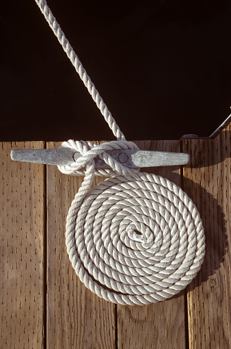 Close-up of standing rigging rope tied to black oiled deadeye with water ripples in background