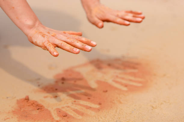 manos de mujer creando formas con arena roja en la playa de estilo arte aborigen - aboriginal art aborigine rock fotografías e imágenes de stock