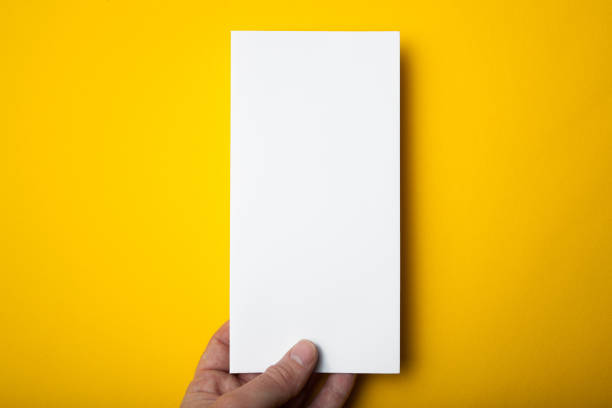 Empty white DL Flyer DL Flyer in hand on yellow background. Mockup. pamphlet stock pictures, royalty-free photos & images