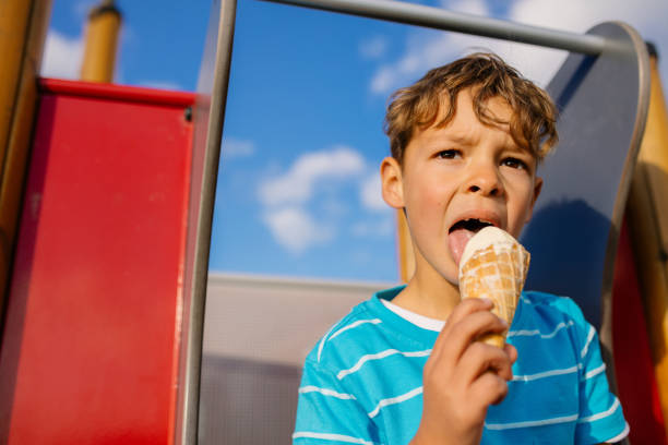 niño comiendo un helado sentados en una diapositiva - ice cream licking little boys ice cream cone fotografías e imágenes de stock