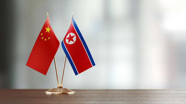 istock Chinese And North Korean Flag Pair On A Desk Over Defocused Background 934242574