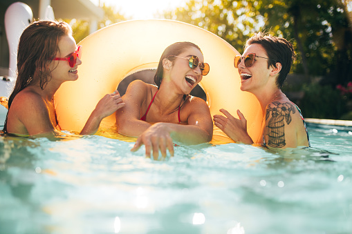 Cheerful women friends laughing and enjoying in swimming pool with inflatable ring. Females having fun in pool party.