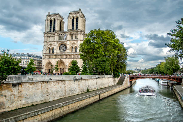 View of Notre-Dame Cathedral on city Sena river bank with cloudy sky and green trees among