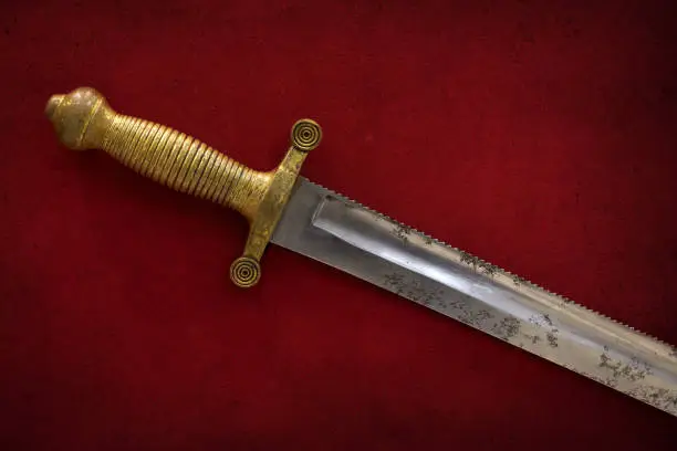 Closeup of a beautiful antique dagger with teeth on the blade and a bronze handle on a vintage red background.