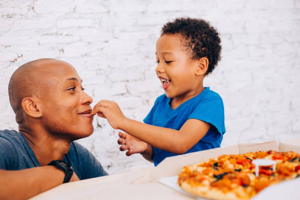 귀여운 작은 아프리카계 미국인 아이 피자와 그의 아버지를 먹이. 따뜻한 가족, 아버지와 아들 관계 - domestic kitchen father eating child 뉴스 사진 이미지