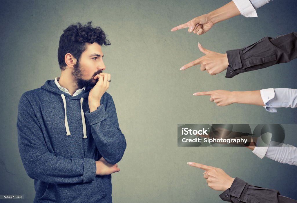 Anxious man judged by different people. Concept of accusation of guilty guy Anxious man judged by different people. Concept of accusation of guilty guy. Negative emotions face expression feeling Envy Stock Photo