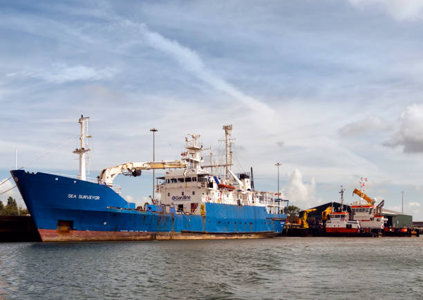 The research-survey vessel ‘Sea Surveyor’ moored next to tugboat utility vessels quayside in the Inner Harbour, Lowestoft, in Suffolk, Eastern England, on a sunny summer day. Belonging to Gardline, one of the world’s largest marine survey companies, the ship is registered in the Bahamas.