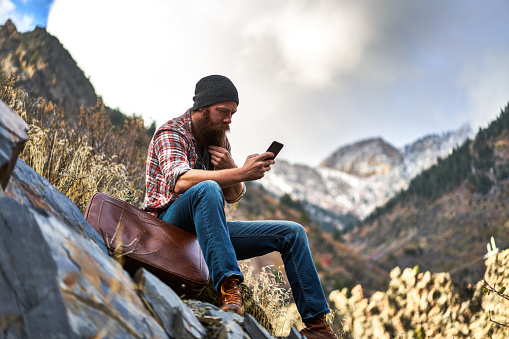 hipster vagabond using smart phone out in the mountains all by himself