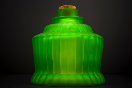 Antique-looking green glass container with cork.  Focus on the bottom half, showing the imperfections of the opaque glass.  Back-lit for effect.  Horizontal composition.