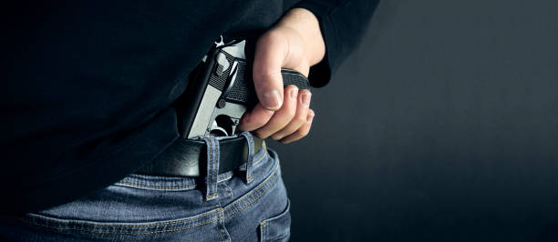istock Terrorist thief man holding gun in his hand. Hidden gun. Isolated on dark background. copy space 934336970