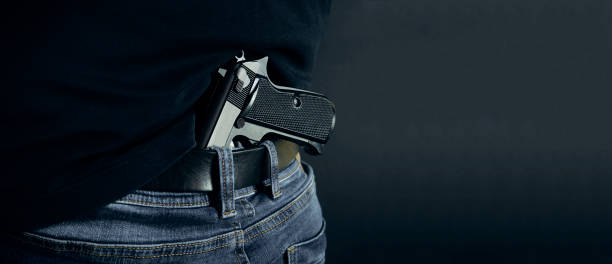 istock Terrorist thief man holding gun in his hand. Hidden gun. Isolated on dark background. copy space 934336972