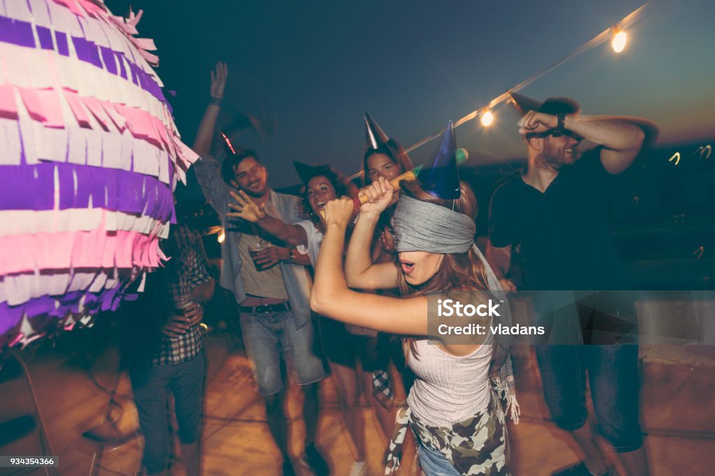 Birthday pinata hitting Birthday girl hitting the pinata with baseball bat while her friends are cheering and laughing. Young people having fun at a rooftop birthday party Piñata Stock Photo