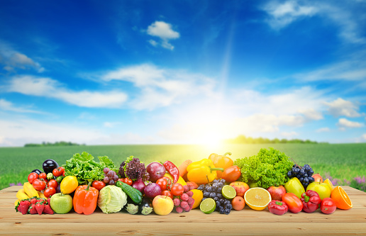 Vegetables and fruit on wooden table of boards against background of spring field and bright blue sky.