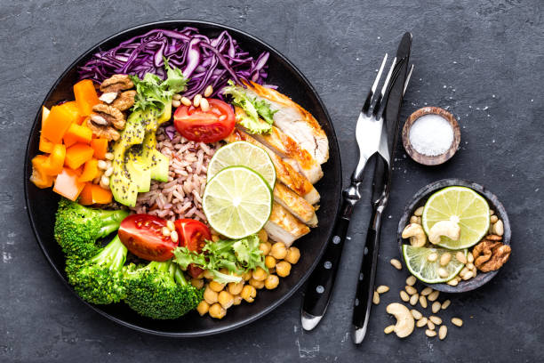 istock Buddha bowl dish with chicken fillet, brown rice, avocado, pepper, tomato, broccoli, red cabbage, chickpea, fresh lettuce salad, pine nuts and walnuts. Healthy balanced eating. Top view 934408306