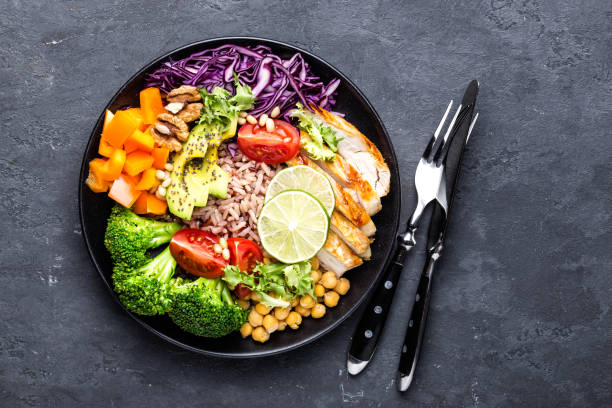 istock Buddha bowl dish with chicken fillet, brown rice, avocado, pepper, tomato, broccoli, red cabbage, chickpea, fresh lettuce salad, pine nuts and walnuts. Healthy balanced eating. Top view 934408462