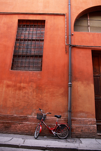 Red bike leaning on a wall. Antique facade in an italian city.