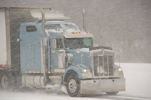 A semi truck travels down a highway during whiteout conditions.