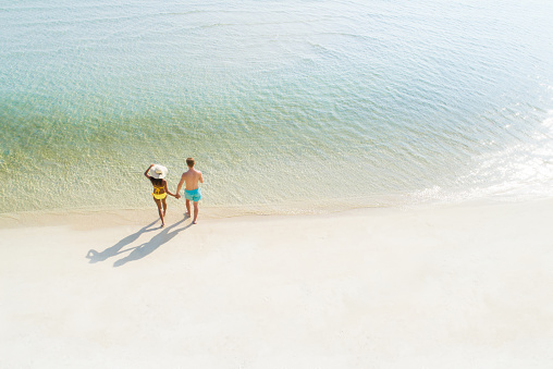 Honeymoon couple holding hand walking on beautiful white sand beach in summer - bird eye view