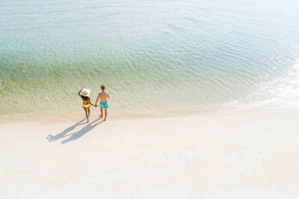 lua de mel casal segurando a mão de andar na bela praia de areia branca no verão - romance honeymoon couple vacations - fotografias e filmes do acervo