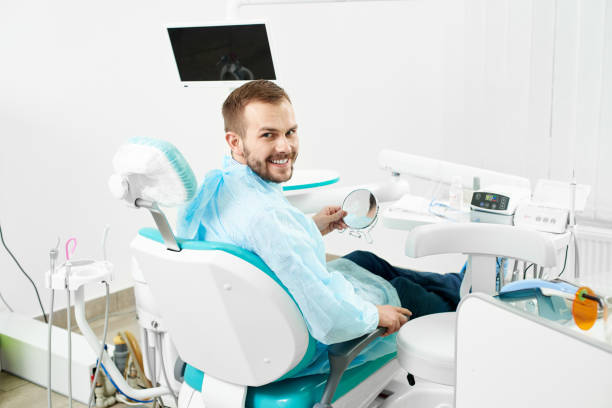 istock Young male client is smiling to the camera while checking his teeth in the mirror in a modern white dentist cabinet. 934491996
