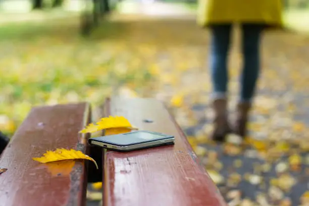 Forgotten smart phone on a park bench. Woman is leaving from a bench where she lost her cell phone.