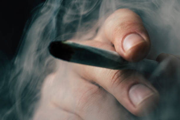 istock A man smokes cannabis weed, a joint and a lighter in his hands. Smoke on a black background. Concepts of medical marijuana use and legalization of the cannabis. 934516258