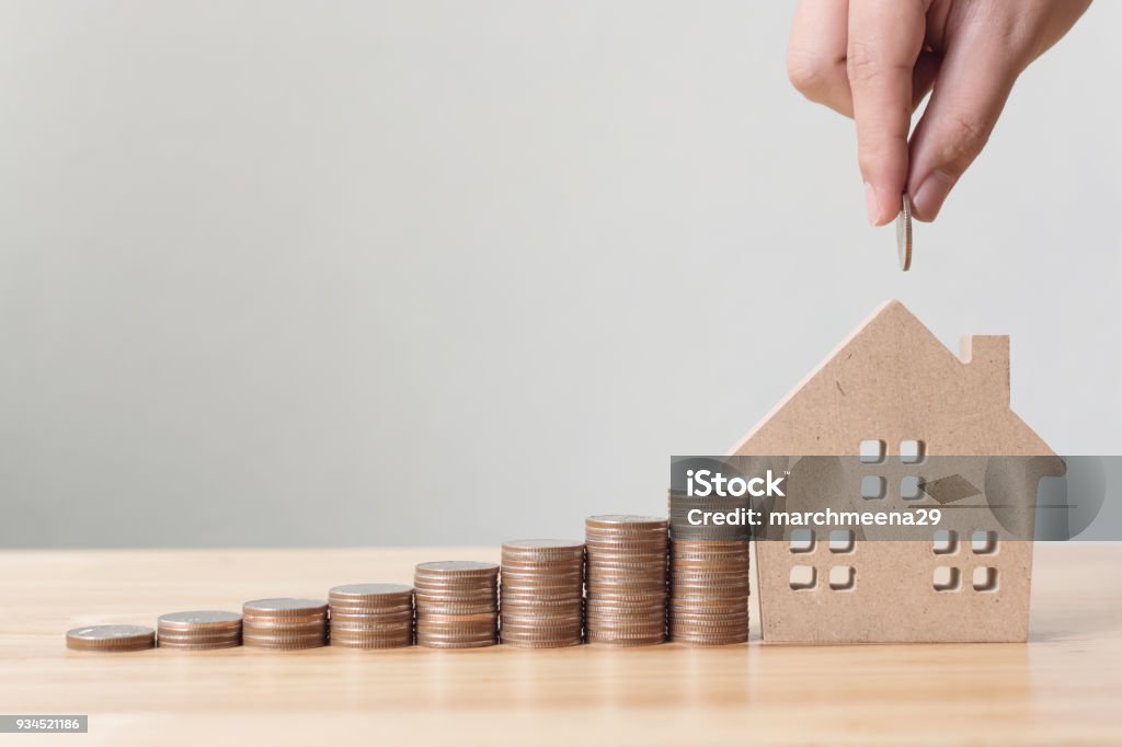 Property investment and house mortgage financial concept, Hand putting money coin stack with wooden house House Stock Photo