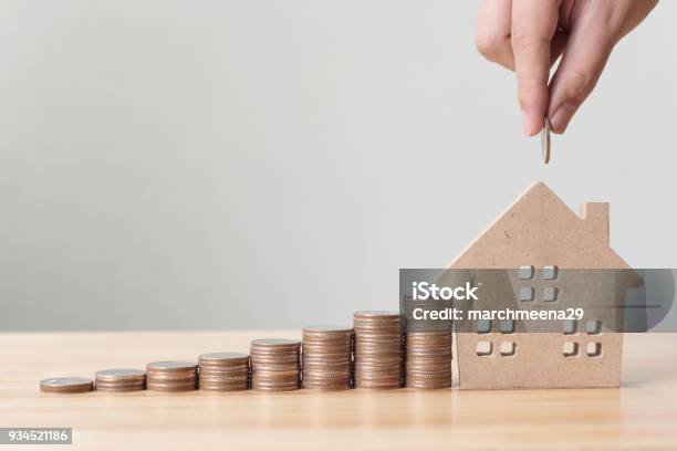 Property Investment And House Mortgage Financial Concept Hand Putting Money Coin Stack With Wooden House Stock Photo - Download Image Now