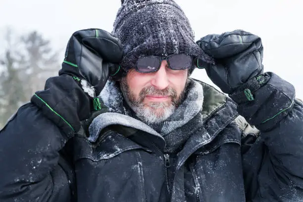 Happy mature man in 50's adjusts his sunglasses that are wet and snowy from four wheeling across a frozen lake on a cold winter day in northern Minnesota, USA
