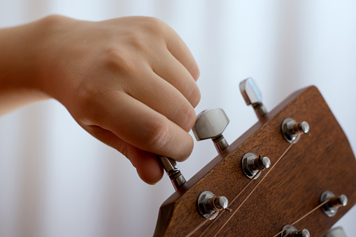 Photo of girl's hand tuning guitar, close-up