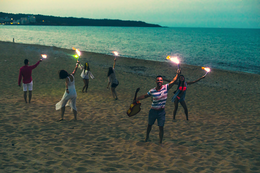 Group of cheerful friends celebrating with fireworks on beach, at night.