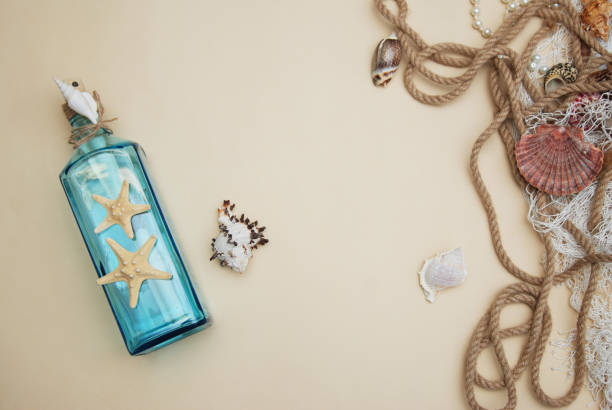 istock Nautical Theme Backdrop, Decorative Bottle with Shells, Starfish on Neutral Ivory Background. Place for text. Selective focus. 934649698