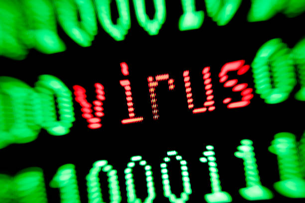 A hand is holding a magnifying glass for a computer screen with all different kinds of computer languages. In the magnifying glass a computer virus is visible.  Focus is on the word VIRUS.