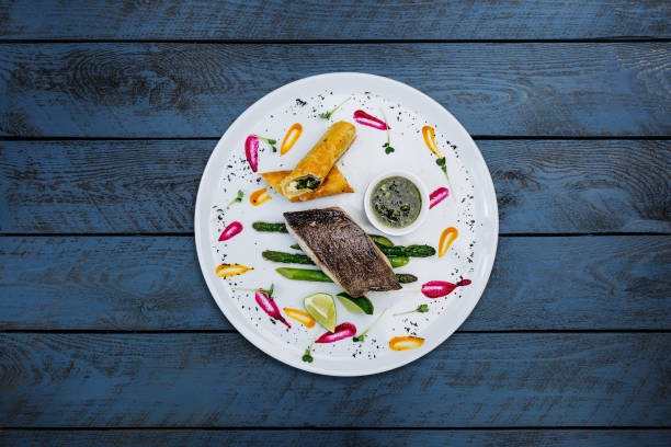 Fillet of black cod with asparagus and cheese with honey-ginger sauce. Fillet of black cod with asparagus and cheese with honey-ginger sauce, served in a ceramic white plate with wooden background. Top view. asparagus organic dinner close to stock pictures, royalty-free photos & images