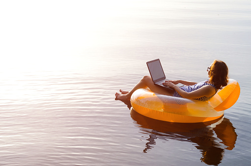 Mujer de negocios trabajando en una laptop en un inflable del anillo en el agua, una copia del espacio libre. Adicto al trabajo, trabajo de vacaciones. photo