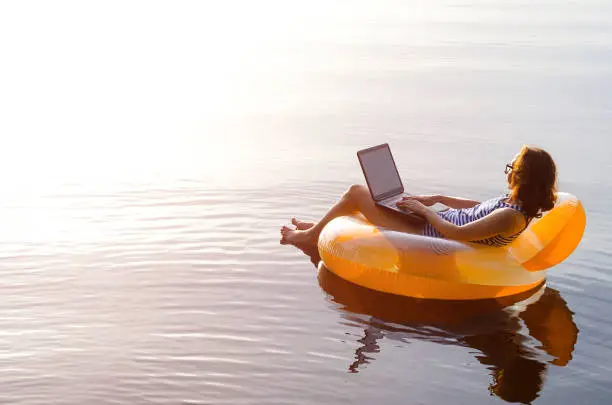 Photo of Business woman working on a laptop in an inflatable ring in the water, a copy of the free space. Workaholic, work on vacation.